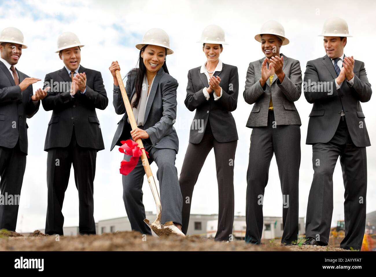 Sorridente di mezza età imprenditrice esegue la cerimonia innovativa di un nuovo sviluppo come i suoi colleghi guardano su felicemente e applaudire. Foto Stock
