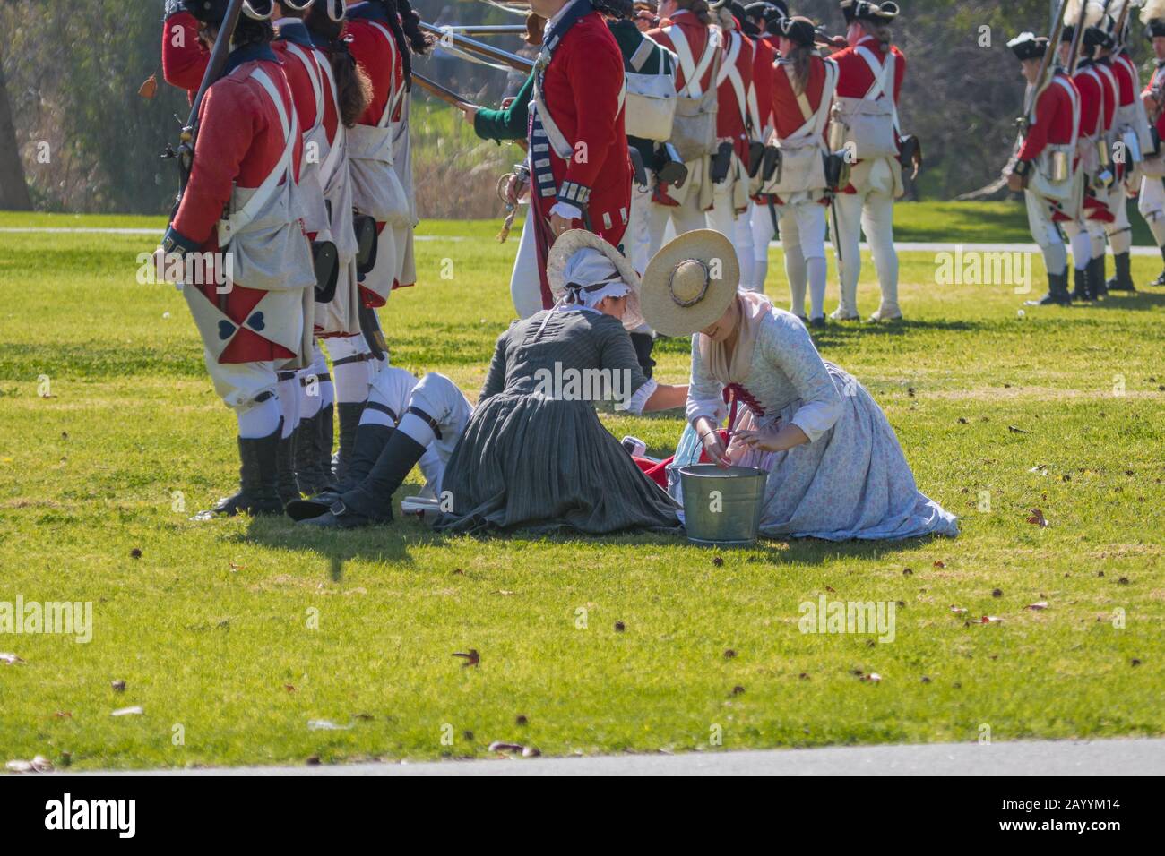 Le donne britanniche curano i soldati feriti del rivestimento rosso durante una rievocazione della rivoluzione americana in un parco Huntington Beach, California, Stati Uniti Foto Stock