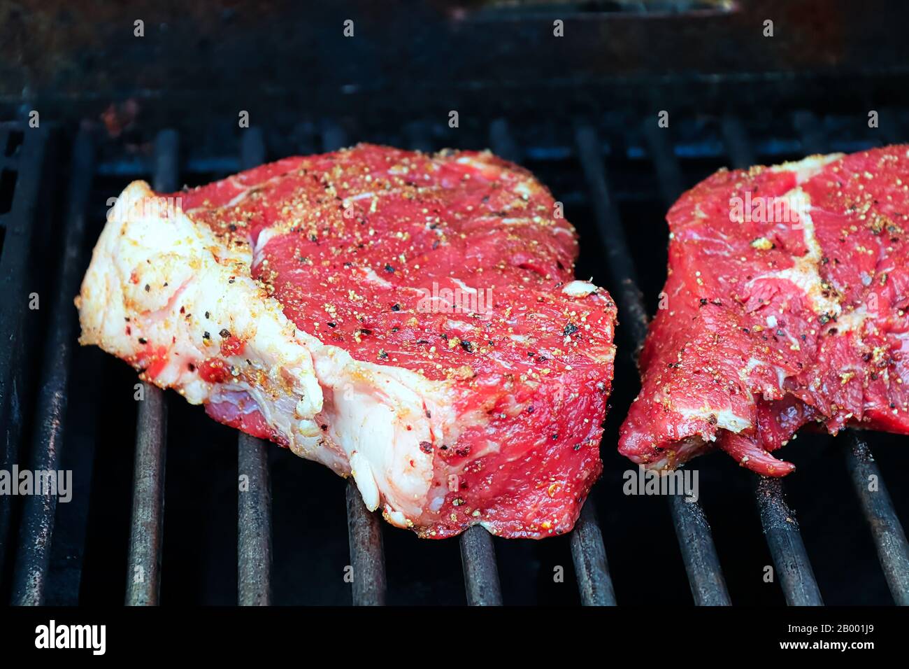 Bistecche crude condite su una griglia barbecue. Foto Stock