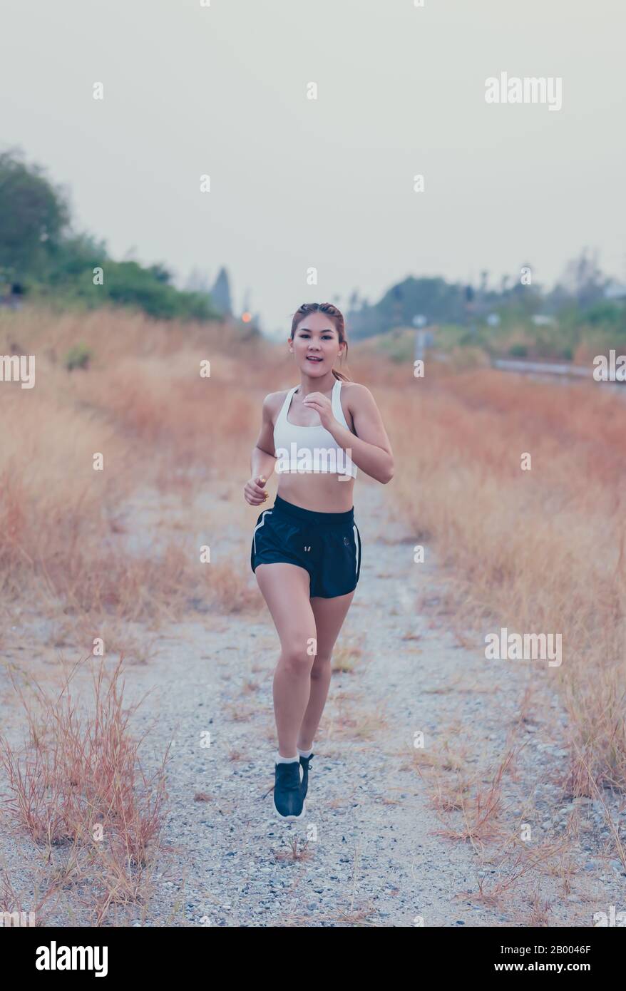 Atleta tailandese donna che corre sulla strada di campagna. Allenamento di resistenza femminile asiatico in estate. Stile di vita heathy e ricreazione sportiva Foto Stock