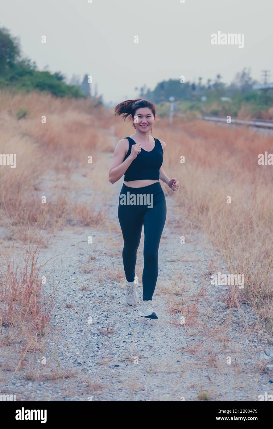 Atleta tailandese donna che corre sulla strada di campagna. Allenamento di resistenza femminile asiatico in estate. Stile di vita heathy e ricreazione sportiva Foto Stock