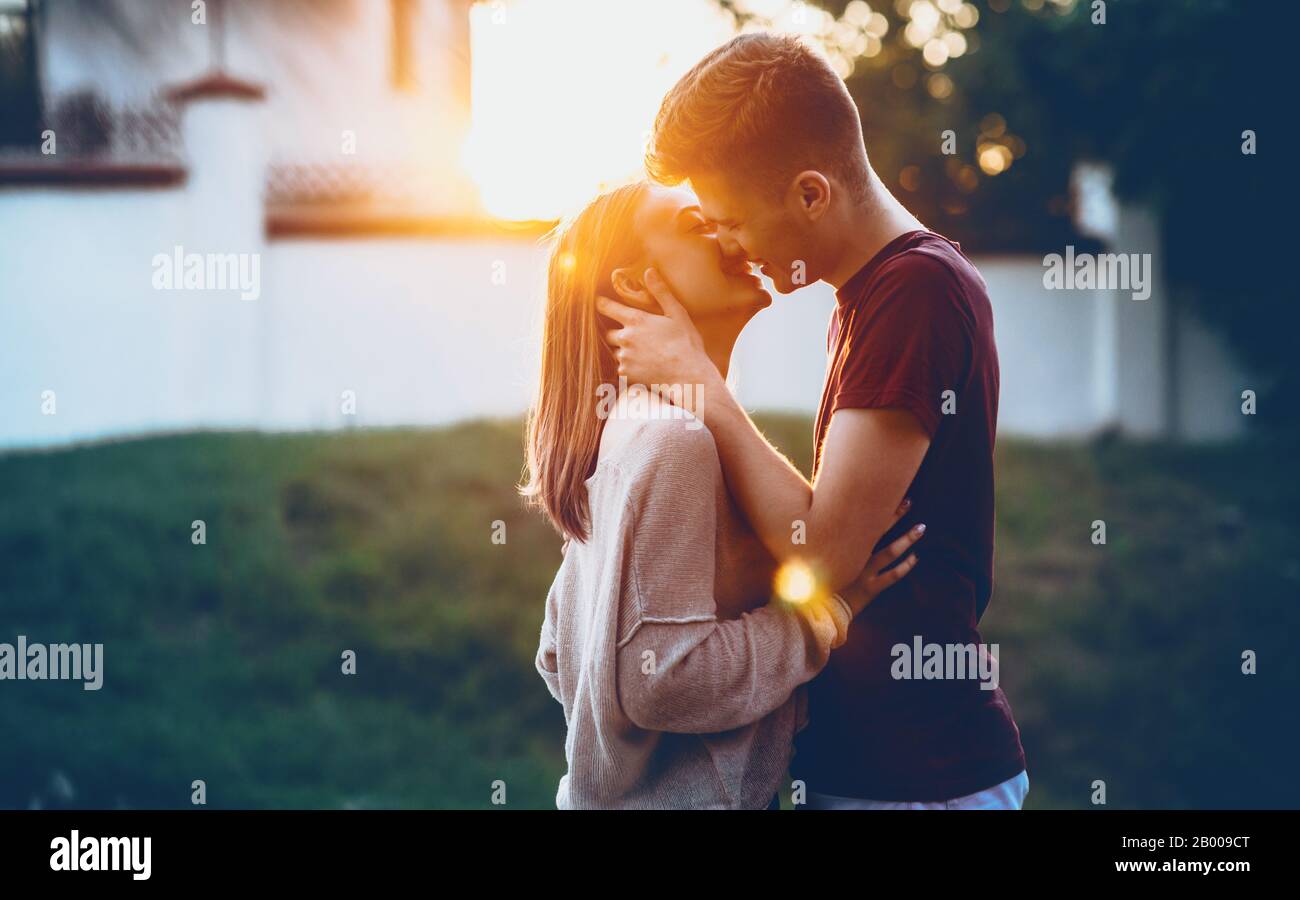 Due sposi caucasici baciano alla luce di un tramonto felice di trascorrere un giorno intero insieme Foto Stock