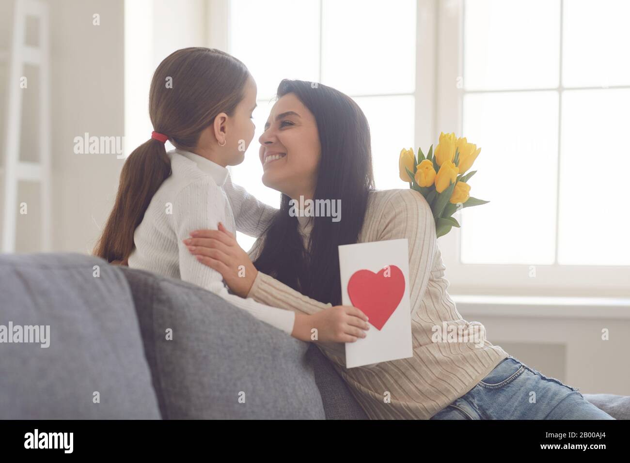 Buon giorno delle madri. La figlia si congratula con sua madre che tiene un mazzo di fiori nella stanza. Foto Stock