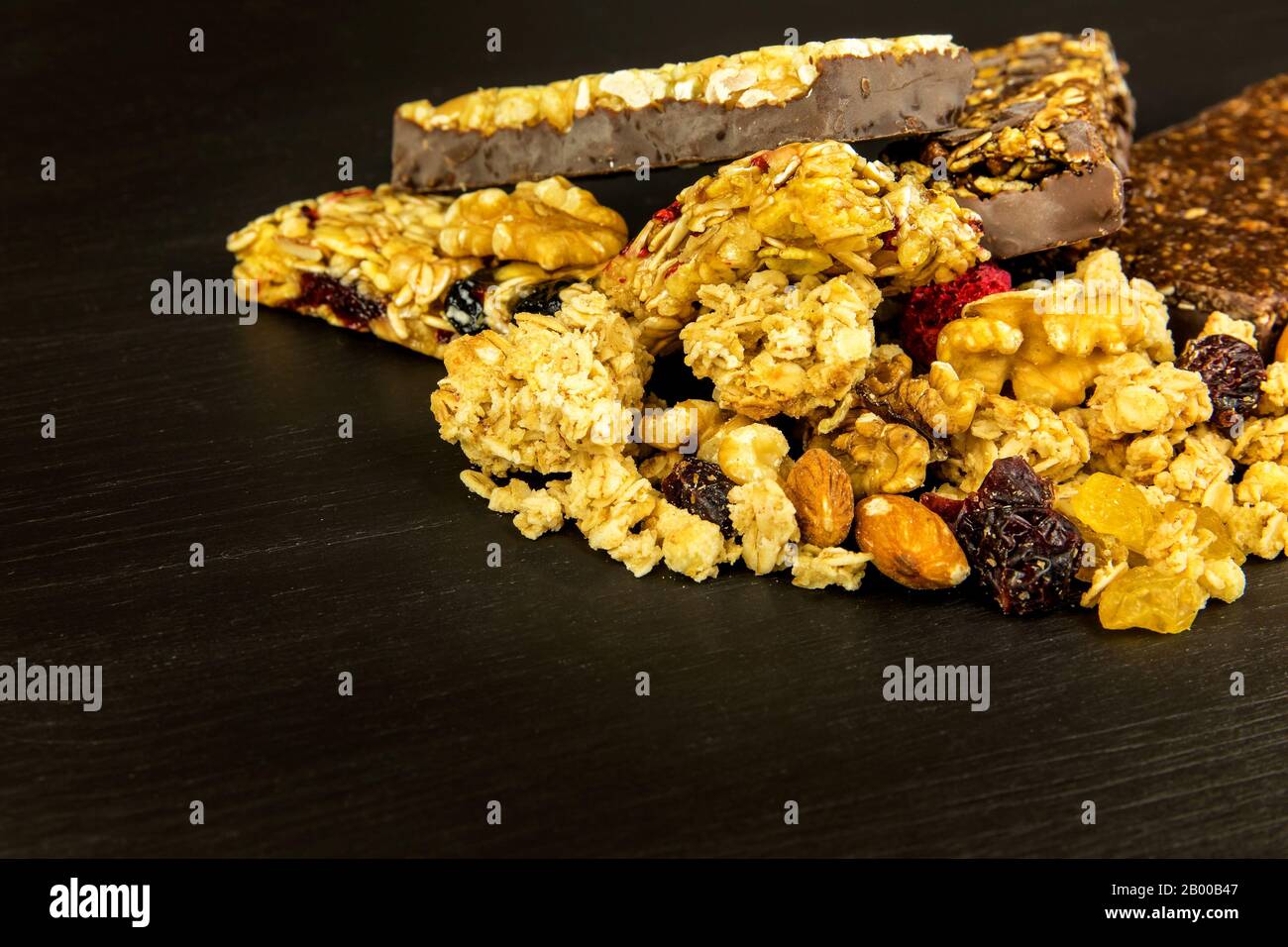 Barrette di granola con noci tostate, fuoco selettivo. Bar con farinata d'avena e noci su sfondo nero. Nutrizione per gli atleti. Dolcezza vegetariana. Foto Stock