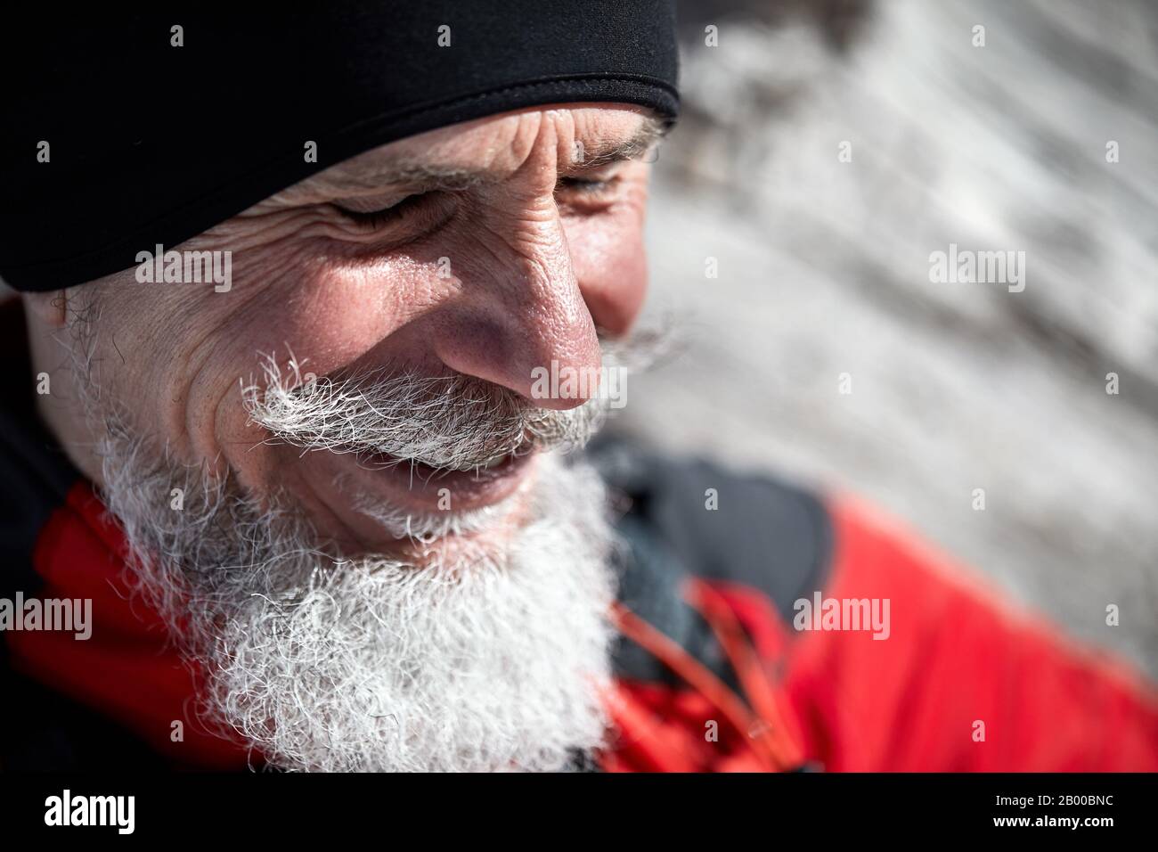 Ritratto di uomo runner anziano con barba grigia sorridente sullo sfondo della montagna invernale Foto Stock