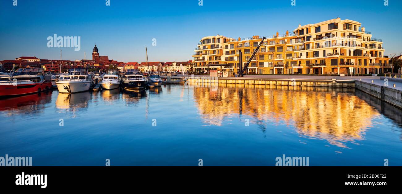 Porto cittadino con moderno complesso alberghiero alla luce della sera, chiesa di San Marien sul retro, Waren an der Mueritz, Mecklenburg Lake District Foto Stock