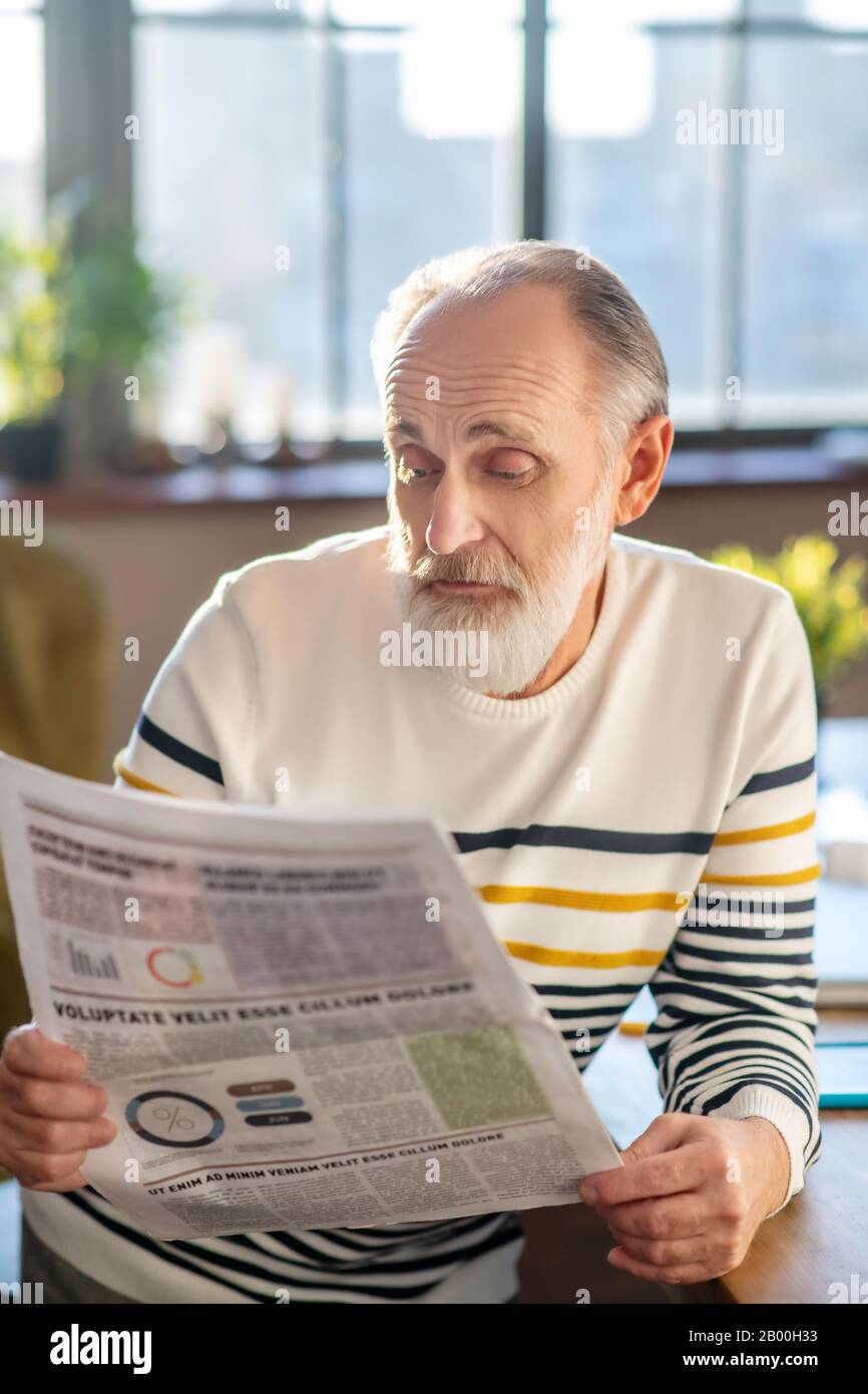 Uomo dai capelli grigi con bearded in maglione a righe che ha un aspetto dubbio Foto Stock