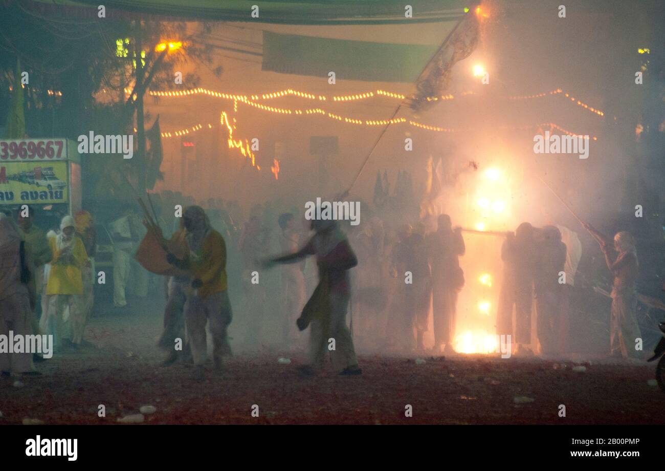 Thailandia: Le strade della città di Phuket esplodendo con i vigili del fuoco come la sfilata passa, Phuket Vegetarian Festival. Il Festival vegetariano è un festival religioso che si tiene ogni anno sull'isola di Phuket, nel sud della Thailandia. Attrae folle di spettatori a causa di molti degli insoliti rituali religiosi che vengono eseguiti. Molti devoti religiosi si schianteranno di spade, perforeranno le loro guance con oggetti taglienti e commetteranno altri atti dolorosi. Foto Stock