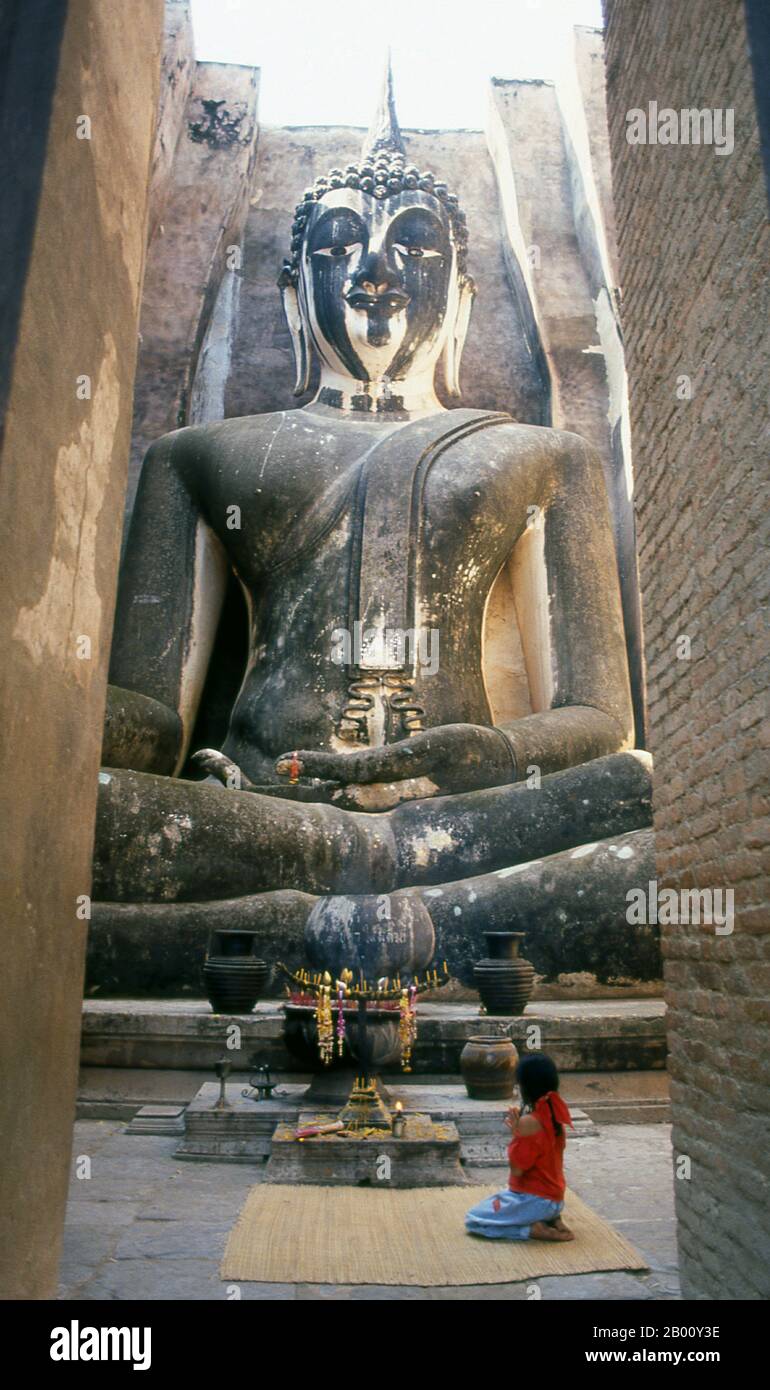 Thailandia: Una giovane ragazza rende omaggio al Buddha seduto alto 15 metri, Wat si Chum, Sukhothai Historical Park. Il Buddha di Phra Atchana a Wat si Chum è nella postura di 'Subduing Maraa' o 'chiamare la Terra a testimoniare'. Sukhothai, che letteralmente significa "Alba della felicità", fu la capitale del regno di Sukhothai e fu fondata nel 1238. Fu la capitale dell'Impero Tailandese per circa 140 anni. Foto Stock