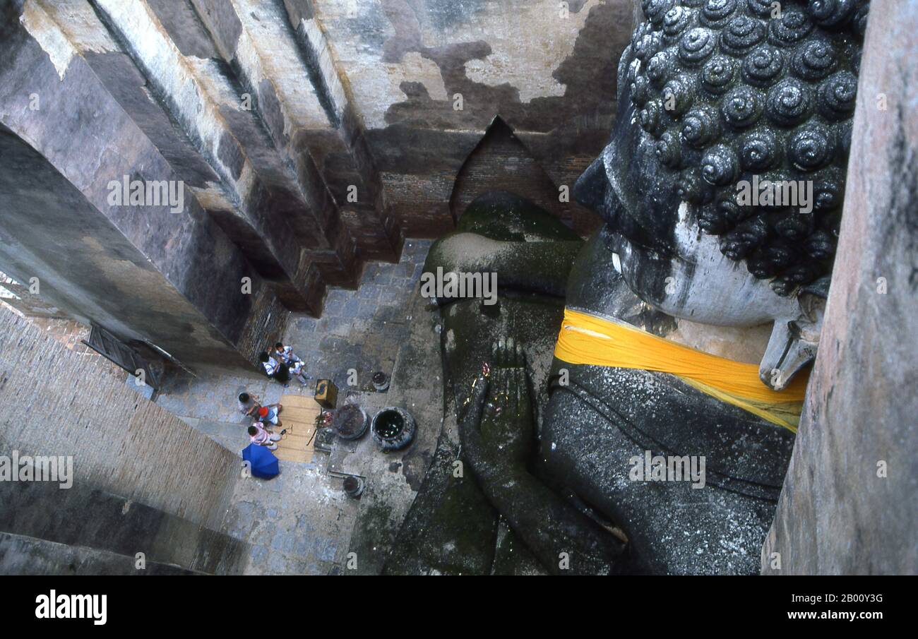 Thailandia: Adorshippers al Buddha seduto alto 15 metri, Wat si Chum, Sukhothai Historical Park. Il Buddha di Phra Atchana a Wat si Chum è nella postura di 'Subduing Maraa' o 'chiamare la Terra a testimoniare'. Sukhothai, che letteralmente significa "Alba della felicità", fu la capitale del regno di Sukhothai e fu fondata nel 1238. Fu la capitale dell'Impero Tailandese per circa 140 anni. Foto Stock