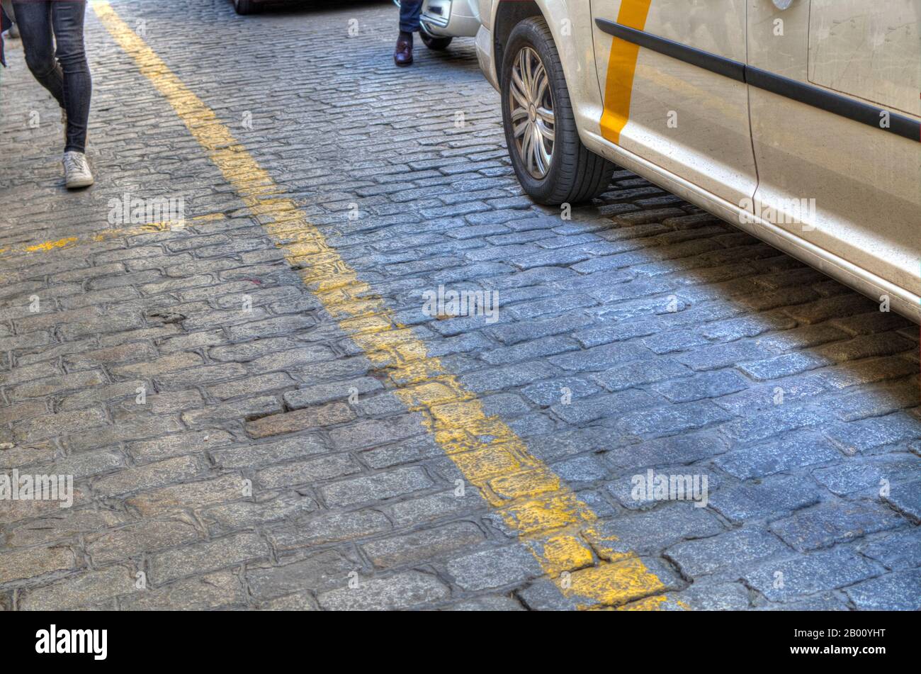 Pavimentazione in ciottoli con linea gialla. Pedoni e veicoli. Siviglia, Spagna. Foto Stock