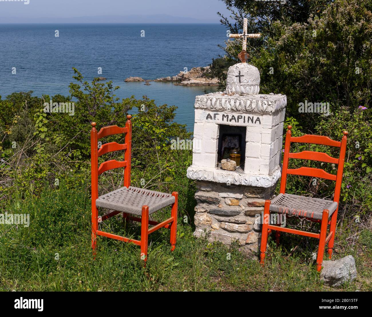 CHALKIDIKI, Grecia - 27 aprile 2019: Cappella di Ikonostasia, cappella greca miniture, lungo la strada con due sedie rosse. Foto Stock