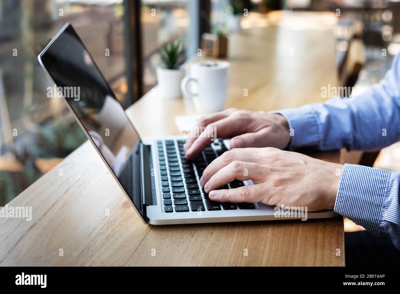 Mani che digitano sulla tastiera del computer portatile, persona che scrive e-mail o rapporto documento in caffè con caffè e internet wifi, stile casual, copia-spazio Foto Stock