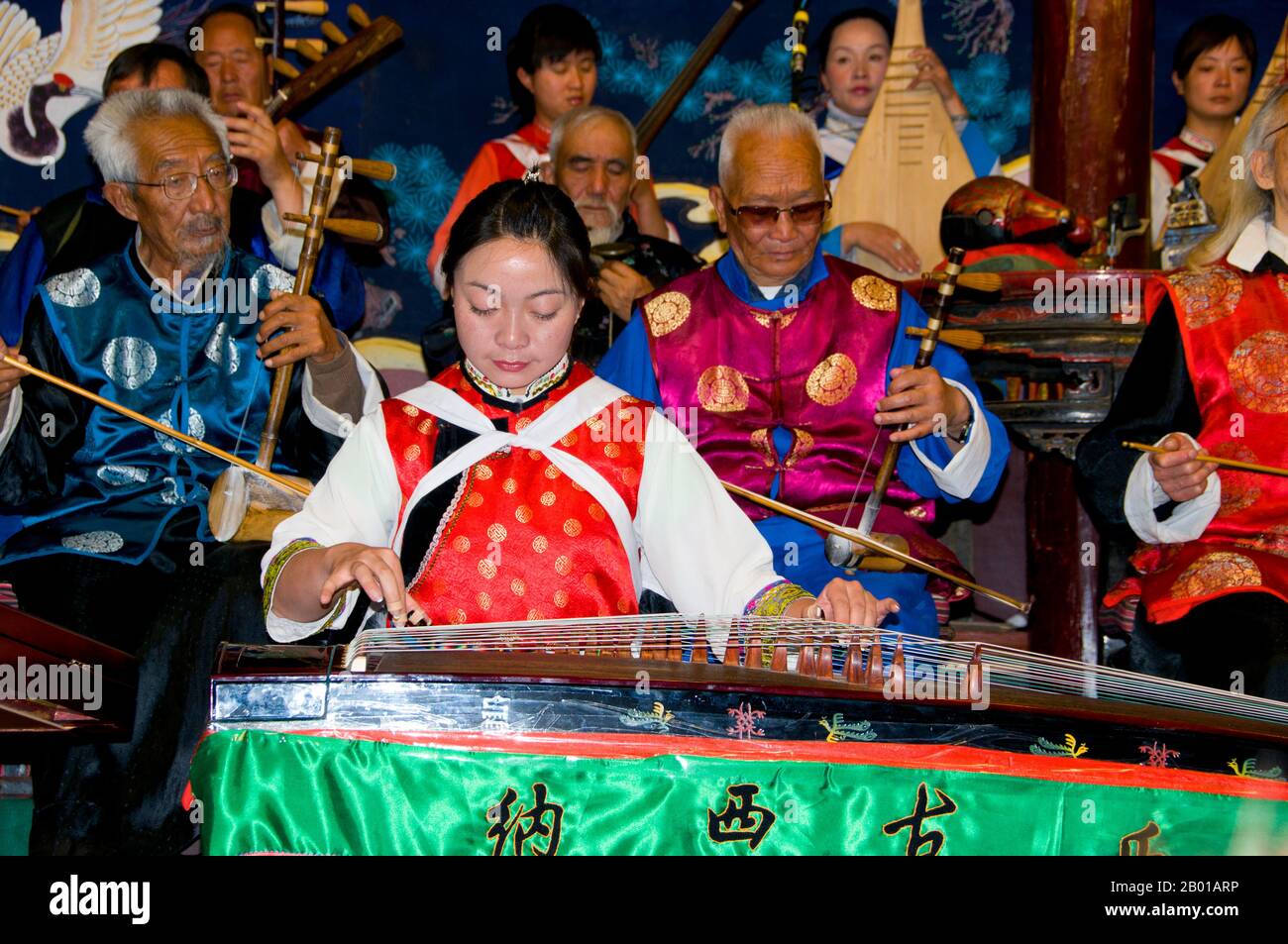 Cina: Una donna scopa un guzheng, la Naxi (Nakhi) Folk Orchestra, Naxi Orchestra Hall, Lijiang Old Town, Yunnan Province. La musica Naxi ha 500 anni e con la sua miscela di testi letterari, argomenti poetici e stili musicali delle dinastie Tang, Song e Yuan, così come alcune influenze tibetane, ha sviluppato il suo stile e i suoi tratti unici. Ci sono tre stili principali: Baisha, Dongjing e Huangjing, tutti utilizzando strumenti tradizionali cinesi. I Naxi o Nakhi sono un gruppo etnico che vive ai piedi delle colline dell'Himalaya nella parte nord-occidentale della provincia di Yunnan. Foto Stock