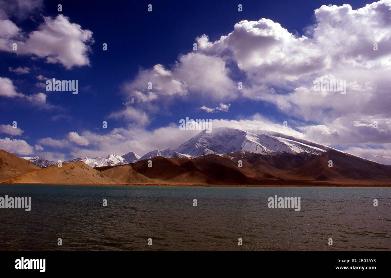 Cina: Muztagh ATA (Ice Mountain Padre) accanto al Lago Karakul sulla Karakoram Highway, Xinjiang. Muztagh ATA, o Muztagata (Uyghur: 'Padre di montagna di ghiaccio'), è il secondo più alto (7546 metri) delle montagne che formano il bordo settentrionale dell'altopiano tibetano (non il secondo più alto delle montagne dell'altopiano tibetano). A volte è considerato come parte del Kunlun Shan, anche se fisicamente è più strettamente collegato ai Pamirs. Si presume inoltre che sia una delle vette più facili da scalare di 7.000 m del mondo, a causa del suo dolce pendio occidentale e del tempo relativamente più secco. Foto Stock