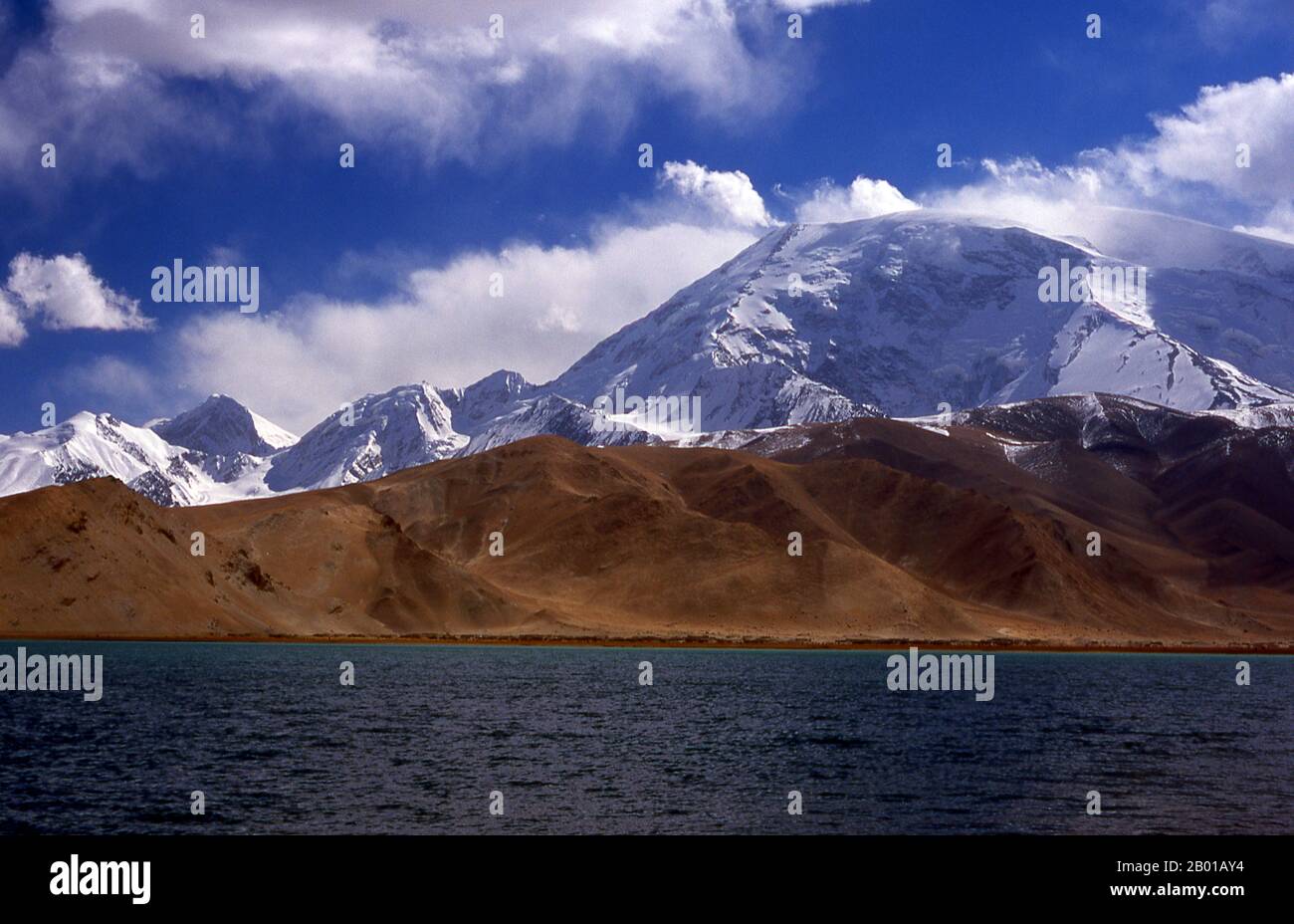 Cina: Muztagh ATA (Ice Mountain Padre) accanto al Lago Karakul sulla Karakoram Highway, Xinjiang. Muztagh ATA, o Muztagata (Uyghur: 'Padre di montagna di ghiaccio'), è il secondo più alto (7546 metri) delle montagne che formano il bordo settentrionale dell'altopiano tibetano (non il secondo più alto delle montagne dell'altopiano tibetano). A volte è considerato come parte del Kunlun Shan, anche se fisicamente è più strettamente collegato ai Pamirs. Si presume inoltre che sia una delle vette più facili da scalare di 7.000 m del mondo, a causa del suo dolce pendio occidentale e del tempo relativamente più secco. Foto Stock