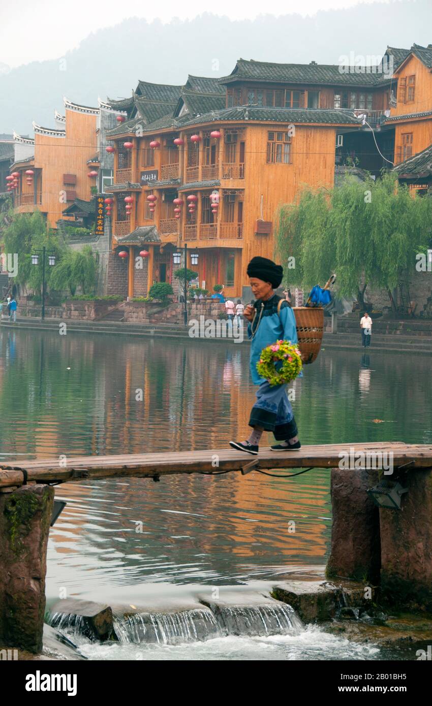 Cina: Donna Tujia sul vecchio ponte di legno attraverso il fiume Tuo, Fenghuang, provincia di Hunan. Fenghuang è cinese per Phoenix e si riferisce al mitico uccello da fuoco sacro che si può trovare nelle mitologie dei Persiani, Greci, Romani, Egiziani, Cinesi, E (secondo Sanchuniathon) i Fenici. La leggenda suggerisce che due phoenixes sulla scoperta della città hovered sopra per un certo tempo considerevole prima di volare riluttante via. Fenghuang è un'antica città ben conservata che risale al 248 a.C. Ospita le minoranze Miao e Tujia. Foto Stock