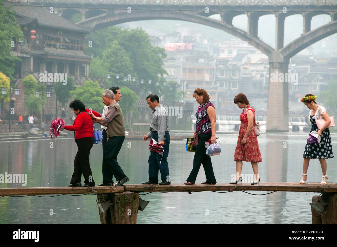 Cina: Attraversando il vecchio ponte di legno attraverso il fiume Tuo, Fenghuang, provincia di Hunan. Fenghuang è cinese per Phoenix e si riferisce al mitico uccello da fuoco sacro che si può trovare nelle mitologie dei Persiani, Greci, Romani, Egiziani, Cinesi, E (secondo Sanchuniathon) i Fenici. La leggenda suggerisce che due phoenixes sulla scoperta della città hovered sopra per un certo tempo considerevole prima di volare riluttante via. Fenghuang è un'antica città ben conservata che risale al 248 a.C. Ospita le minoranze Miao e Tujia. Foto Stock