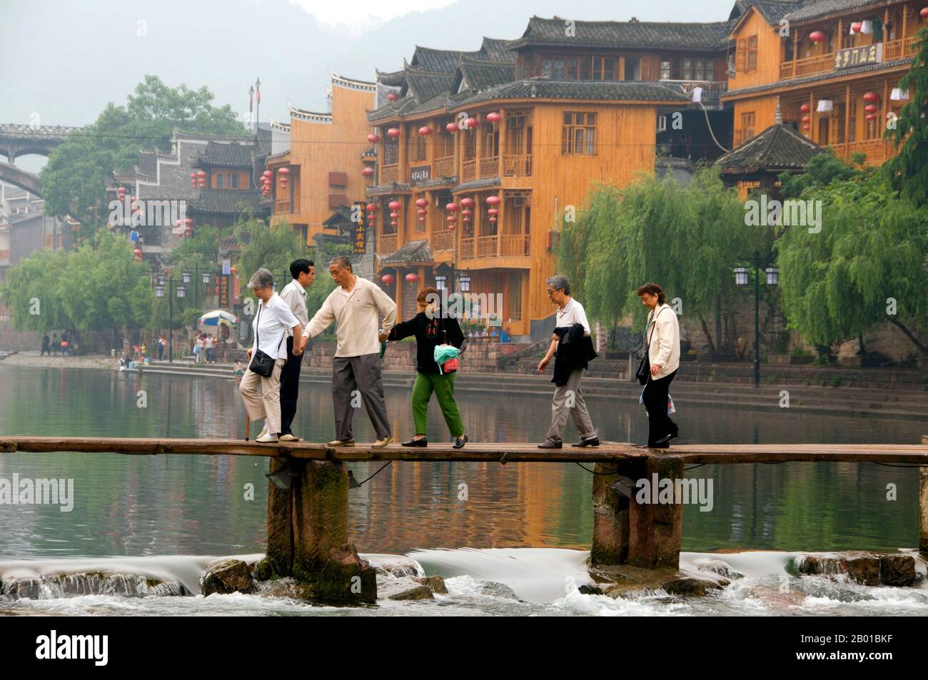 Cina: Attraversando il vecchio ponte di legno attraverso il fiume Tuo, Fenghuang, provincia di Hunan. Fenghuang è cinese per Phoenix e si riferisce al mitico uccello da fuoco sacro che si può trovare nelle mitologie dei Persiani, Greci, Romani, Egiziani, Cinesi, E (secondo Sanchuniathon) i Fenici. La leggenda suggerisce che due phoenixes sulla scoperta della città hovered sopra per un certo tempo considerevole prima di volare riluttante via. Fenghuang è un'antica città ben conservata che risale al 248 a.C. Ospita le minoranze Miao e Tujia. Foto Stock