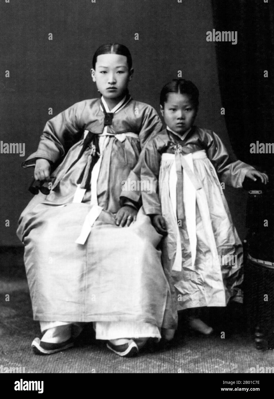 Una giovane donna coreana posa con sua figlia indossando tradizionale abito hanbok, c.. 1910. Hanbok (Corea del Sud) o Chosŏn-ot (Corea del Nord) è l'abito tradizionale coreano. È spesso caratterizzata da colori vivaci e linee semplici senza tasche. Anche se il termine letteralmente significa 'abbigliamento coreano', hanbok oggi spesso si riferisce specificamente a hanbok della dinastia Joseon ed è indossato come abbigliamento semi-formale o formale durante i festival e le celebrazioni tradizionali. Il moderno hanbok non segue esattamente lo stile attuale come indossato nella dinastia Joseon come ha subito alcuni cambiamenti importanti nel 20th ° secolo. Foto Stock