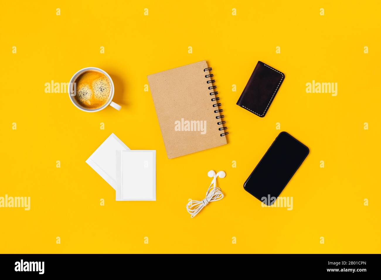 Desktop da ufficio su sfondo giallo con smartphone, blocco note, caffè, immagine polaroide, cuffie. Foto Stock