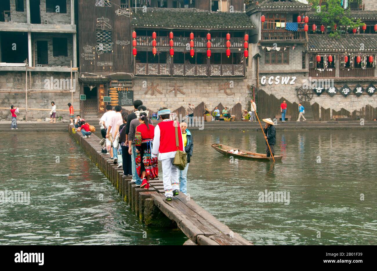 Cina: Attraversando il vecchio ponte di legno attraverso il fiume Tuo, Fenghuang, provincia di Hunan. Fenghuang è cinese per Phoenix e si riferisce al mitico uccello da fuoco sacro che si può trovare nelle mitologie dei Persiani, Greci, Romani, Egiziani, Cinesi, E (secondo Sanchuniathon) i Fenici. La leggenda suggerisce che due phoenixes sulla scoperta della città hovered sopra per un certo tempo considerevole prima di volare riluttante via. Fenghuang è un'antica città ben conservata che risale al 248 a.C. Ospita le minoranze Miao e Tujia. Foto Stock