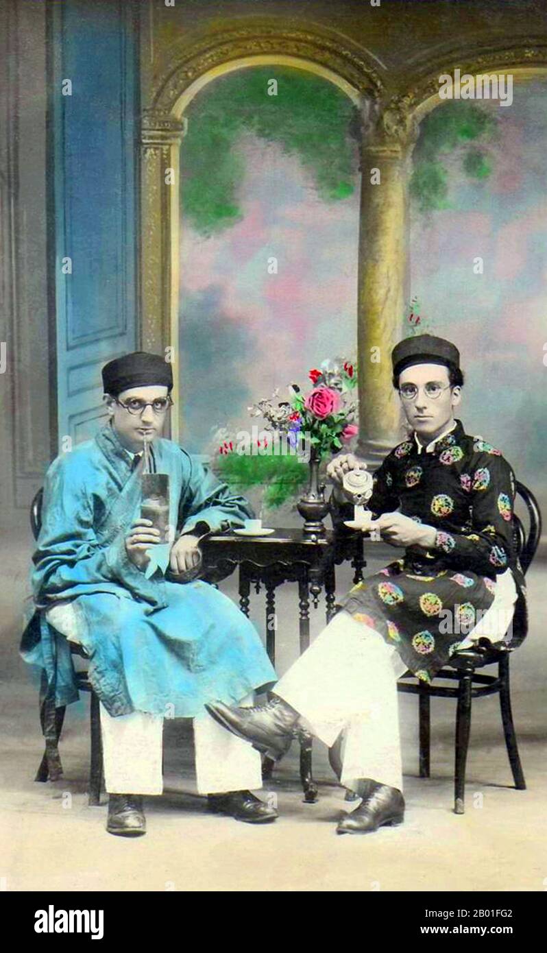 Vietnam: Due uomini seduti, probabilmente Parsis o ebrei indiani, indossando gli uomini di ao dai o vietnamita 'vestito lungo', Hanoi, 1910. L'ao dai (vietnamita: áo dài) è un costume nazionale vietnamita, ora più comunemente per le donne. Nella sua forma attuale, è una tunica di seta aderente indossata sui pantaloni. La parola è pronunciata [ǎːwzâːj]. Áo deriva da una parola cinese centrale che significa 'cappotto imbottito' (襖). Dài significa 'lungo'. La parola 'ao dai' fu originariamente applicata al vestito indossato alla corte dei signori Nguyễn a Huế nel 18th ° secolo. Questo abito si è evoluto nel áo ngũ thân. Foto Stock