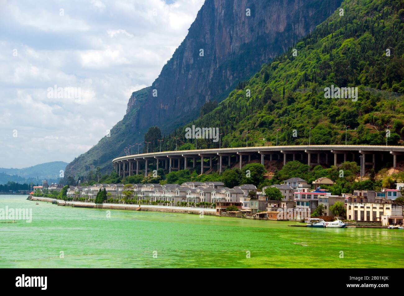 Cina: Autostrada che corre sotto le colline occidentali (Xishan), vicino a Kunming, provincia dello Yunnan. Il lago Dian o lago Kunming è un grande lago interterrestre situato sull'altopiano dello Yunnan-Guizhou vicino a Kunming, nella provincia dello Yunnan. Il suo soprannome è "Sparkling Pearl Embedded in a Highland", ed è stato il modello per il lago Kunming nel Palazzo estivo di Pechino. Si tratta di un lago di faglia d'acqua dolce a 1.886,5 m (6.189 piedi) sul livello del mare. Il lago copre 298 km2 (115 miglia quadrate). È lunga 39 km da nord a sud, e la profondità media è di 4,4 m (14 ft). È l'ottavo lago più grande della Cina. Foto Stock