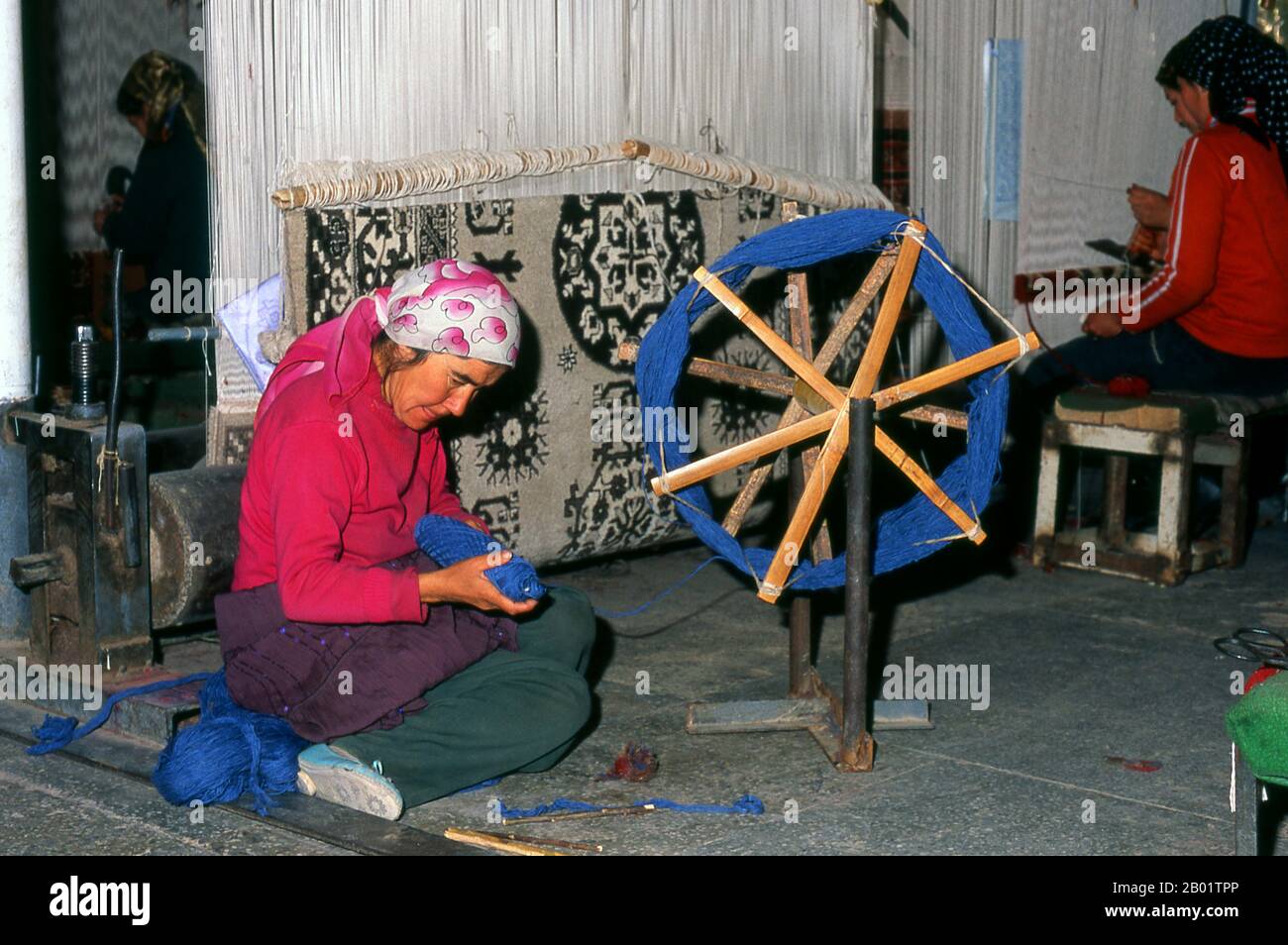 Cina: Tessitori di tappeti uiguri, fabbrica di tappeti, Khotan, Xinjiang. Khotan traccia la sua storia almeno fino al III secolo a.C., quando si dice che il figlio maggiore dell'imperatore indiano Asoka si sia insediato qui. Era di grande importanza sulla via della seta, e si dice che sia stato il primo posto fuori dalla Cina ad aver coltivato seta. Si trova a cavallo dei fiumi Karakash o «Giada Nera» e Yurungkash o «Giada Bianca», che qui si uniscono per formare il Khotan Darya, ed è famoso per la sua giada da oltre due millenni. Foto Stock