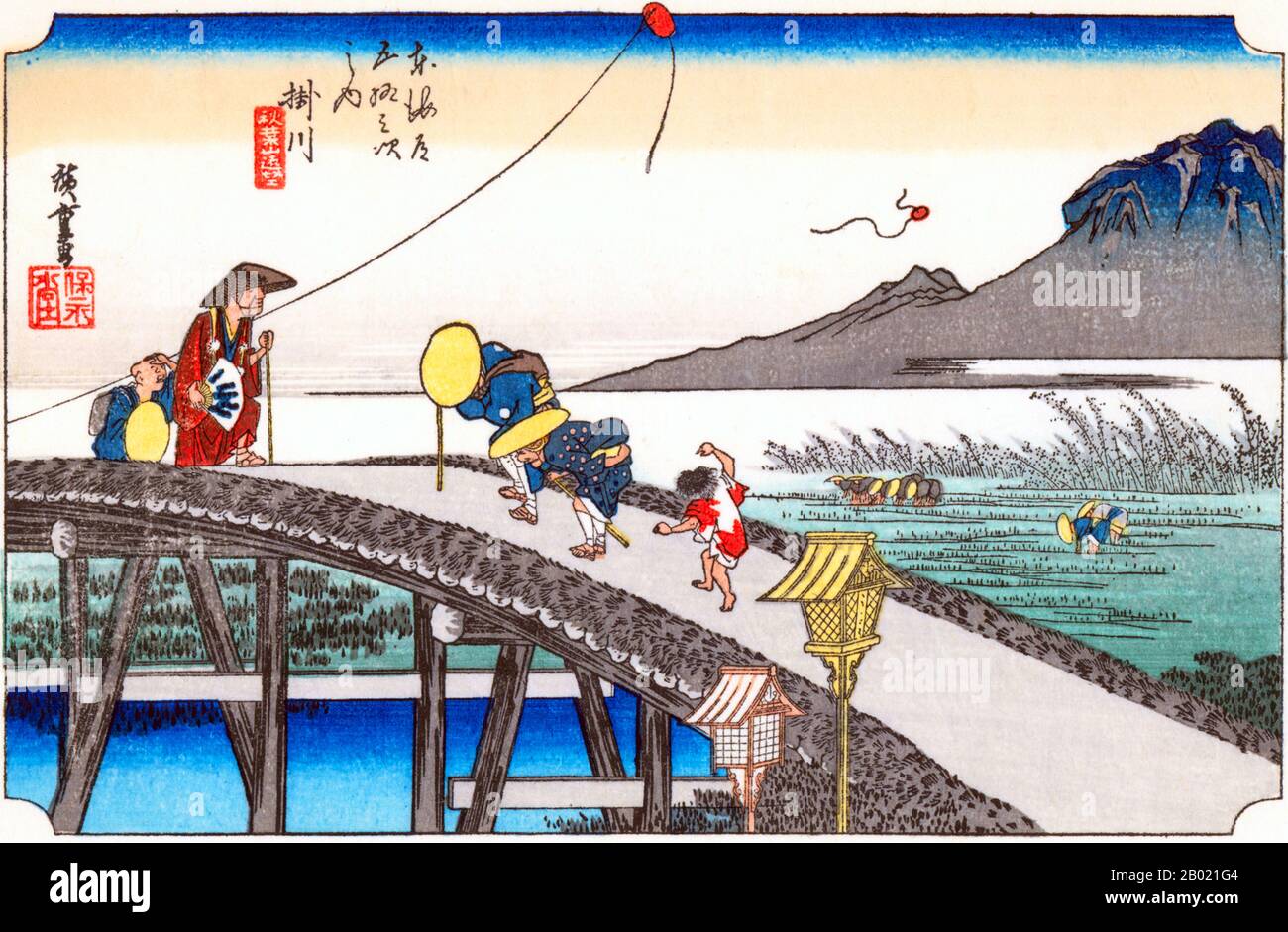 Giappone: "Stazione ventisei: Kakegawa, Monte Akiha". Ukiyo-e xilografia della serie '53 stazioni della strada Tôkaidô' di Utagawa Hiroshige (1797-1858), 1834 circa. Kakegawa: Viaggiatori che attraversano un alto ponte sul fiume Kake, due di loro sbirciano nell'acqua sottostante, e dietro un ragazzino che guarda un aquilone in aria, mentre oltre un altro, con la corda rotta, fluttua verso terra. Contadini che trapiantano riso nei campi allagati e in lontananza il Monte Akiba che si innalza sopra le nebbie. Foto Stock