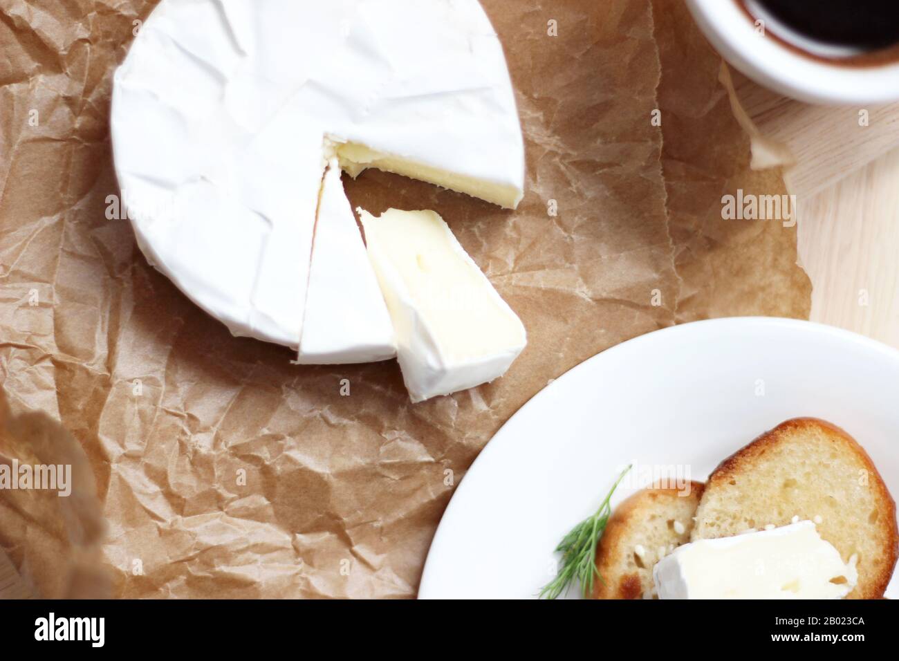 Formaggio francese. Formaggio Brie in carta da imballaggio sul tavolo con Toast e tazza di caffè. Stile degli alimenti. Prodotti francesi tradizionali. Foto Stock