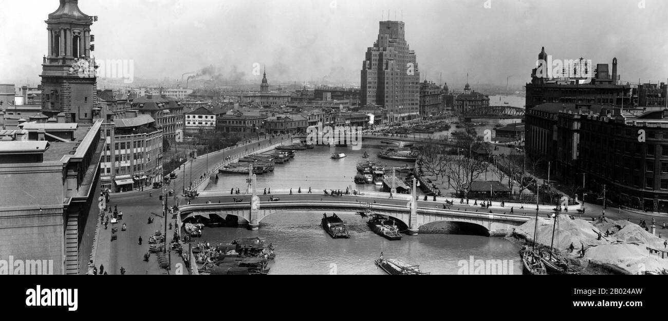 Cina: Shanghai, guardando verso sud lungo il Suzhou Creek, oltre il ponte Waibaidu fino al fiume Huangpu. Camini fumanti e la maggior parte dell'edificio di Broadway Mansions in lontananza, circa 1935. Il ponte Waibaidu, chiamato Garden Bridge in inglese, è il primo ponte interamente in acciaio, e l'unico esempio sopravvissuto di un ponte a capriata camelback, in Cina. Il quarto ponte straniero costruito nella sua posizione dal 1856, a valle dell'estuario del Suzhou Creek, vicino alla sua confluenza con il fiume Huangpu e adiacente al Bund nel centro di Shanghai, e che collega i distretti di Huangpu e Hongkou. Foto Stock