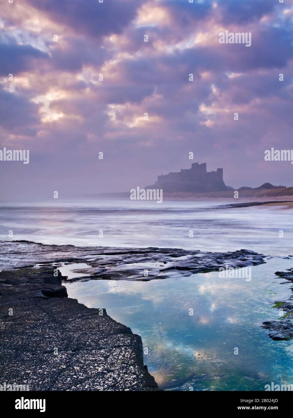 Il castello di Bamburgh alla prima luce da una pedana Whin ripiano di roccia a nord del castello, Northumberland, Inghilterra Foto Stock