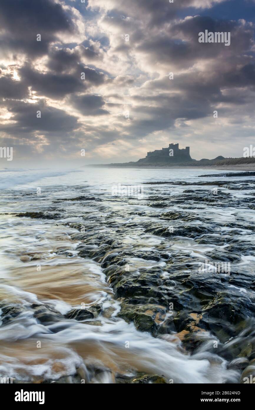 Il castello di Bamburgh alla prima luce da una pedana Whin ripiano di roccia a nord del castello, Northumberland, Inghilterra Foto Stock