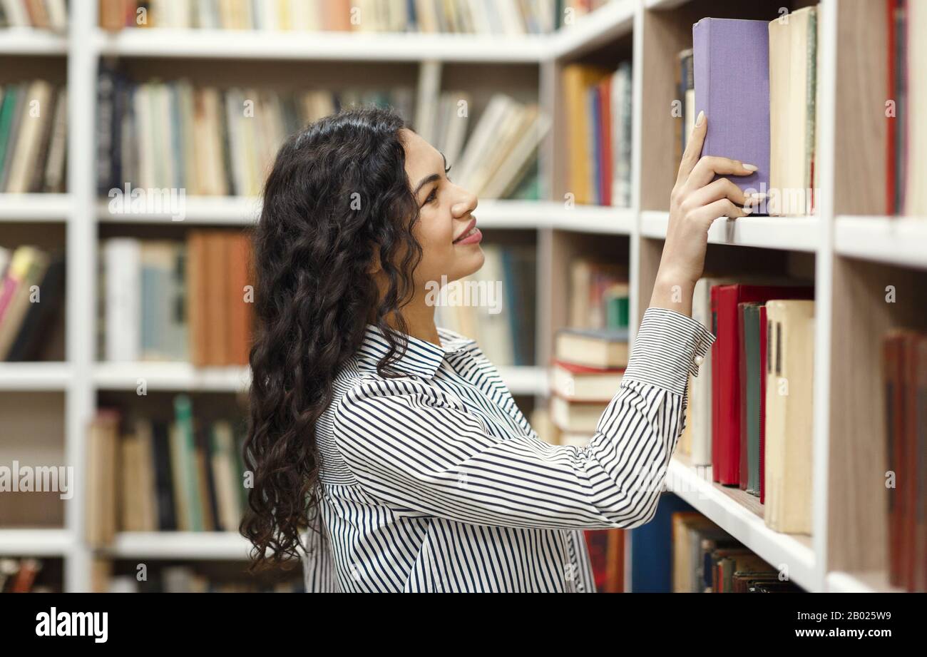 Donna latina sorridente che prende il libro alla biblioteca Foto Stock