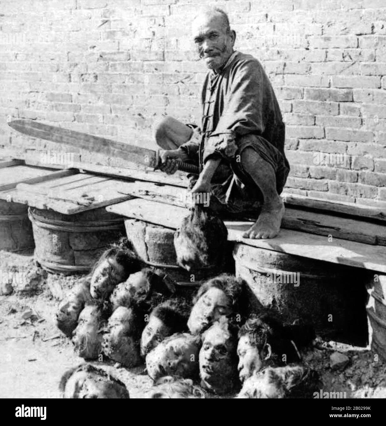 Cina: Un boia, o "capo”, con la sua spada e una collezione di teste mozzate. Foto scattata in una prigione di Canton (Guangzhou), tardo periodo Qing, c. 1900. Durante la dinastia Qing, la giustizia penale era basata sul codice legale estremamente dettagliato del grande Qing. Un elemento del sistema giudiziario penale cinese tradizionale è l'idea che il diritto penale abbia uno scopo morale, uno dei quali è quello di far pentire i condannati e vedere l'errore dei loro metodi. Nel sistema giuridico tradizionale, una persona non può essere condannata per un reato se non ha confessato, portando spesso all'uso della tortura. Foto Stock
