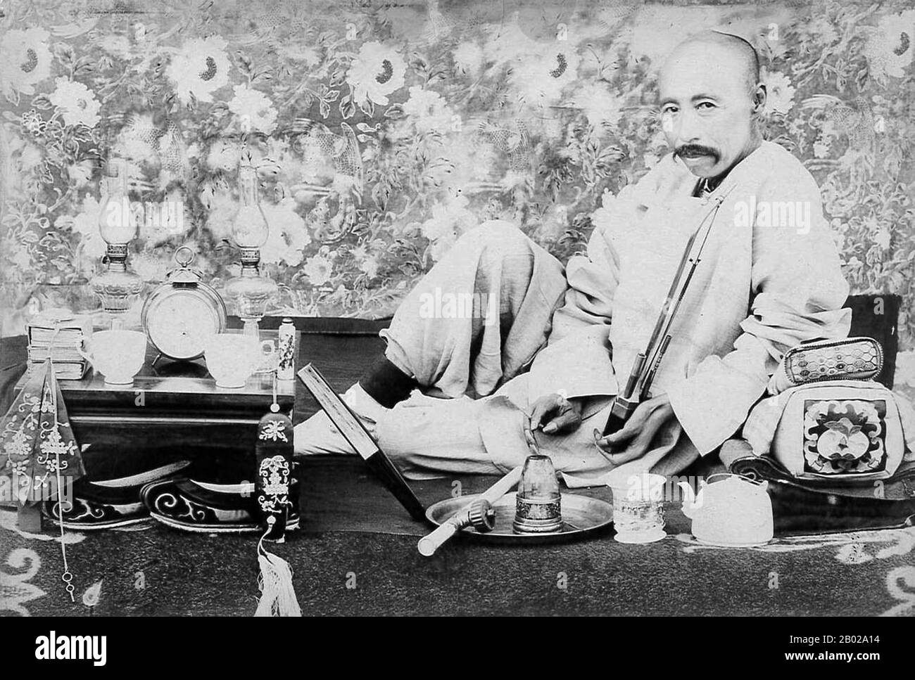 Cina: Un fumatore di oppio che si rilassa con attrezzature da oppio, teiera e pipa del tabacco, 1910 circa. Papavero da oppio, Papaver somniferum, è la specie di pianta da cui vengono estratti oppio e semi di papavero. L'oppio è la fonte di molti oppiacei, tra cui morfina, tebaina, codeina, papaverina e noscapina. Il nome botanico latino significa "papavero che porta il sonno", riferendosi alle proprietà sedative di alcuni di questi oppiacei. Foto Stock