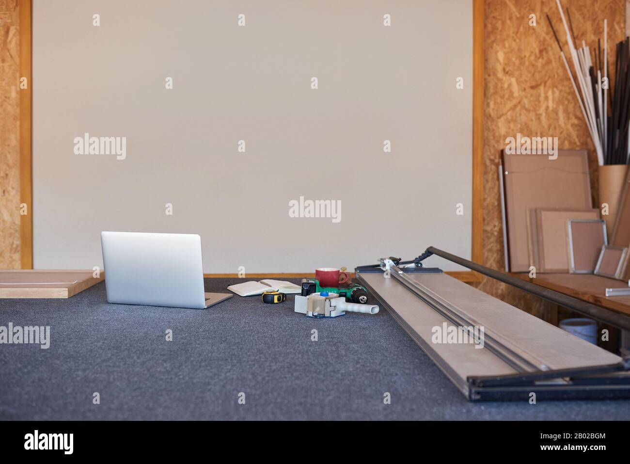 Taglierina per tappeti e computer portatile su un tavolo da lavoro per l'incorniciatura Foto Stock