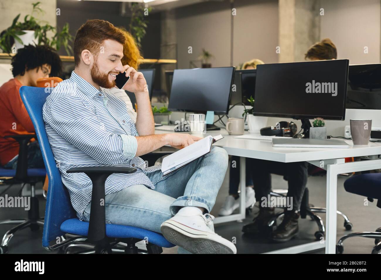 Giovane uomo che discute documento finanziario con il cliente per telefono Foto Stock