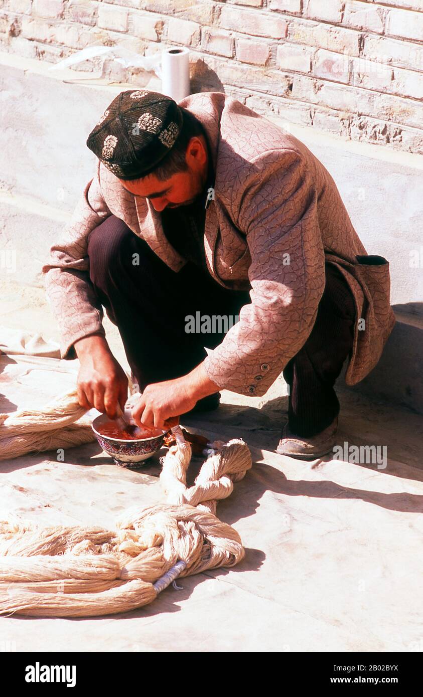 Cina: Un uomo uiguro che immerge fili di seta crudi, Atlas Silk Workshop (Atlas Karakhana) nel villaggio di Jiya, a circa 13 km a nord-est di Khotan, provincia dello Xinjiang. Durante la prima metà del i secolo d.C., si pensa che la tecnologia dei vermi da seta abbia raggiunto l'oasi dominata dagli Han-cinesi di Khotan nel bacino del Tarim - un'oasi che è ancora oggi un centro di produzione della seta. Si dice che una principessa cinese data in matrimonio con un principe Khotan abbia portato le uova di bachi da seta al suo nuovo marito nascoste nei suoi capelli. Foto Stock