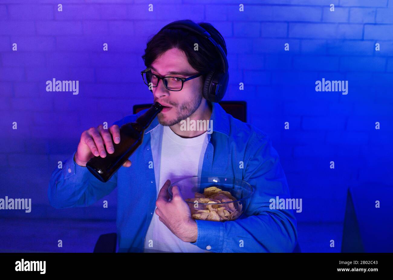 Millennial Guy Giocando Gioco Online Bere Birra A Casa, A Bassa Luce Foto Stock