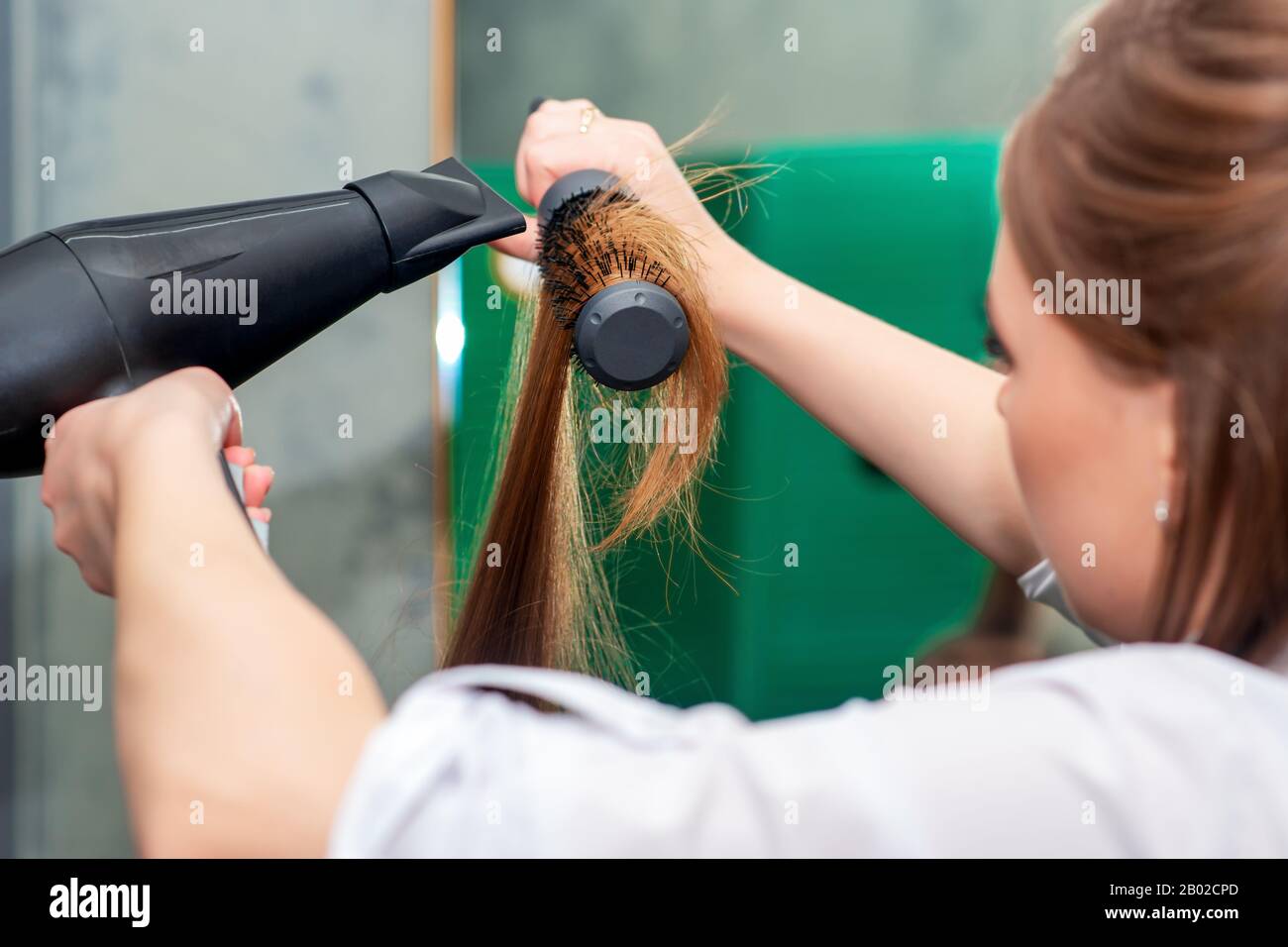 Parrucchiere che asciuga capelli castani lunghi con asciugacapelli e  spazzola rotonda, primo piano Foto stock - Alamy