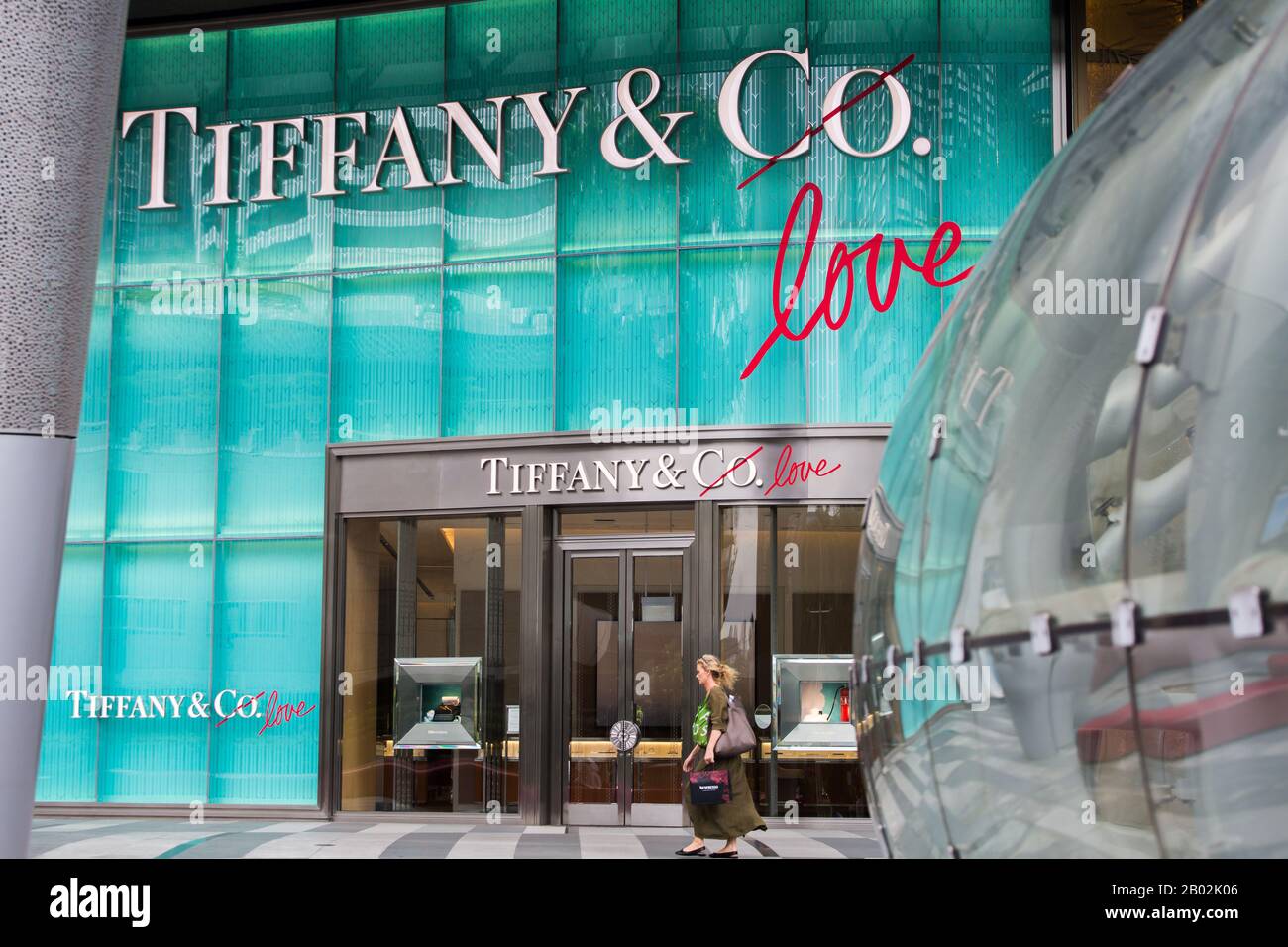 Una donna occidentale con una borsa passava davanti a un boutique di lusso di alta classe a Orchard ION, Singapore Foto Stock