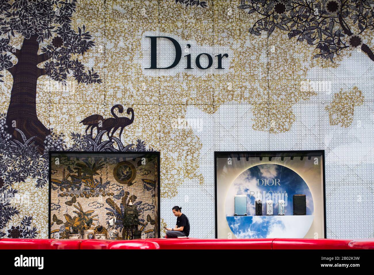 Una persona asiatica siede all'esterno di un lussuoso negozio boutique Christian Dior con esposizione di prodotti presso Orchard ION, Orchard Road. Singapore Foto Stock