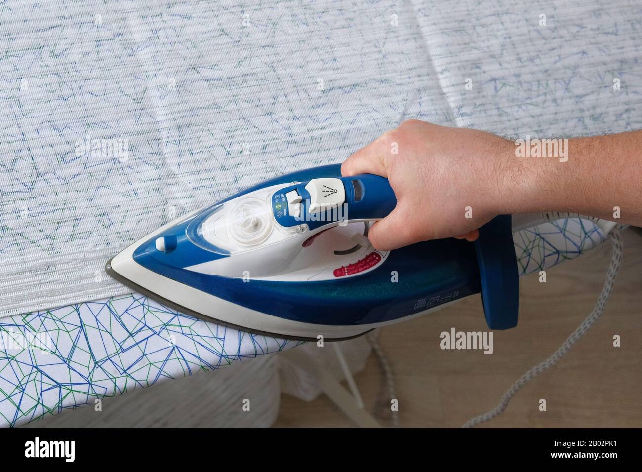 Stiratura di abiti a casa. Marito che fa stiratura dell'abbigliamento in camera. La mano maschile è tessile da stiro, primo piano. Foto Stock