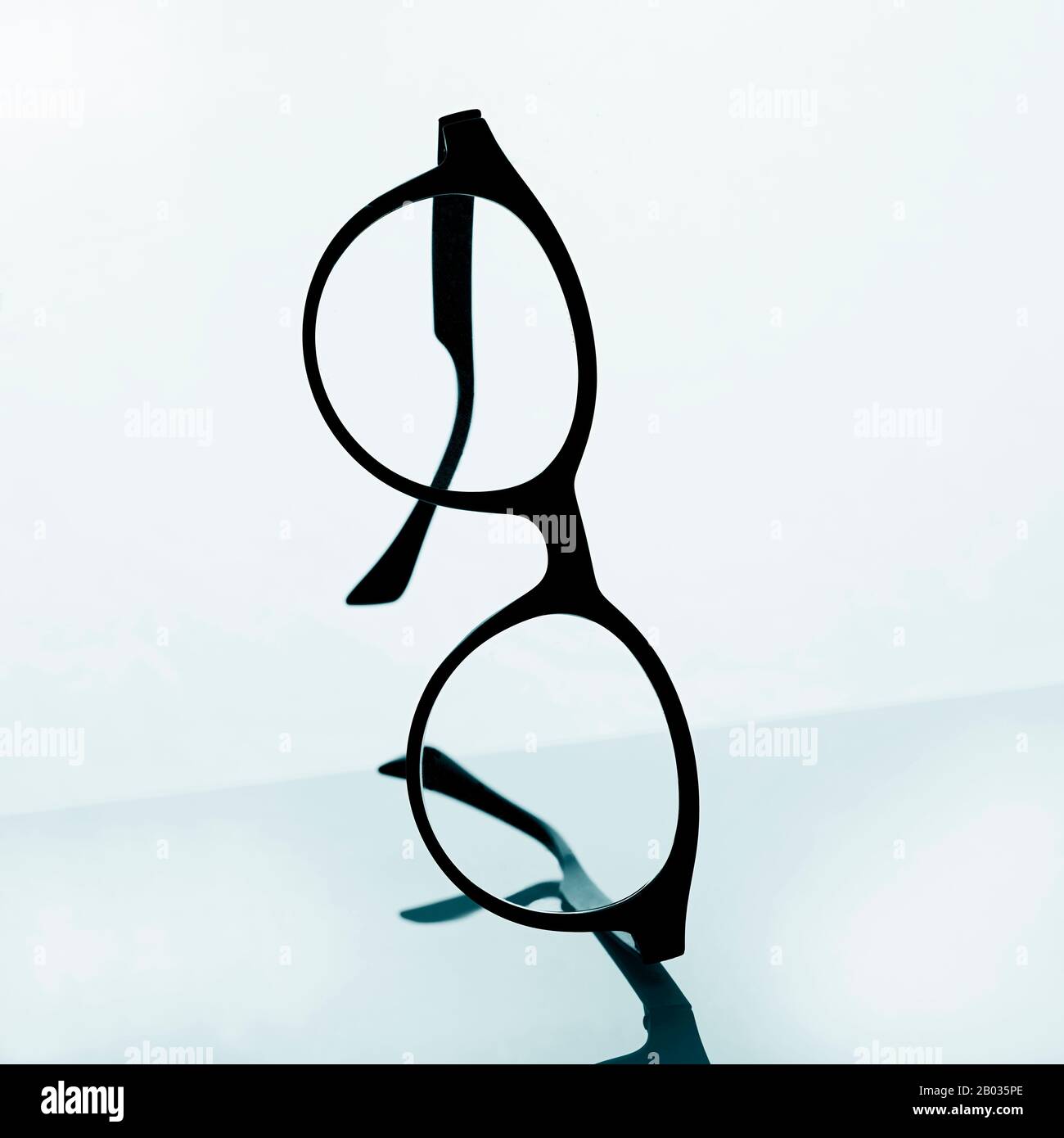 primo piano di un paio di occhiali neri su una superficie riflettente su sfondo bianco Foto Stock