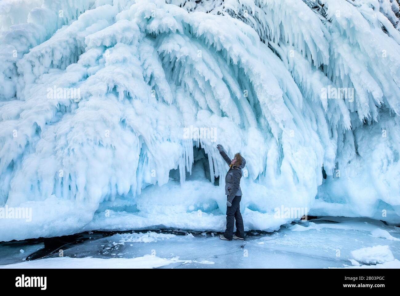Donna che si è meravigliata del massiccio muro di ghiaccio formato come risultato di onde e vento. Lago Baikal, Siberia, Russia. Foto Stock