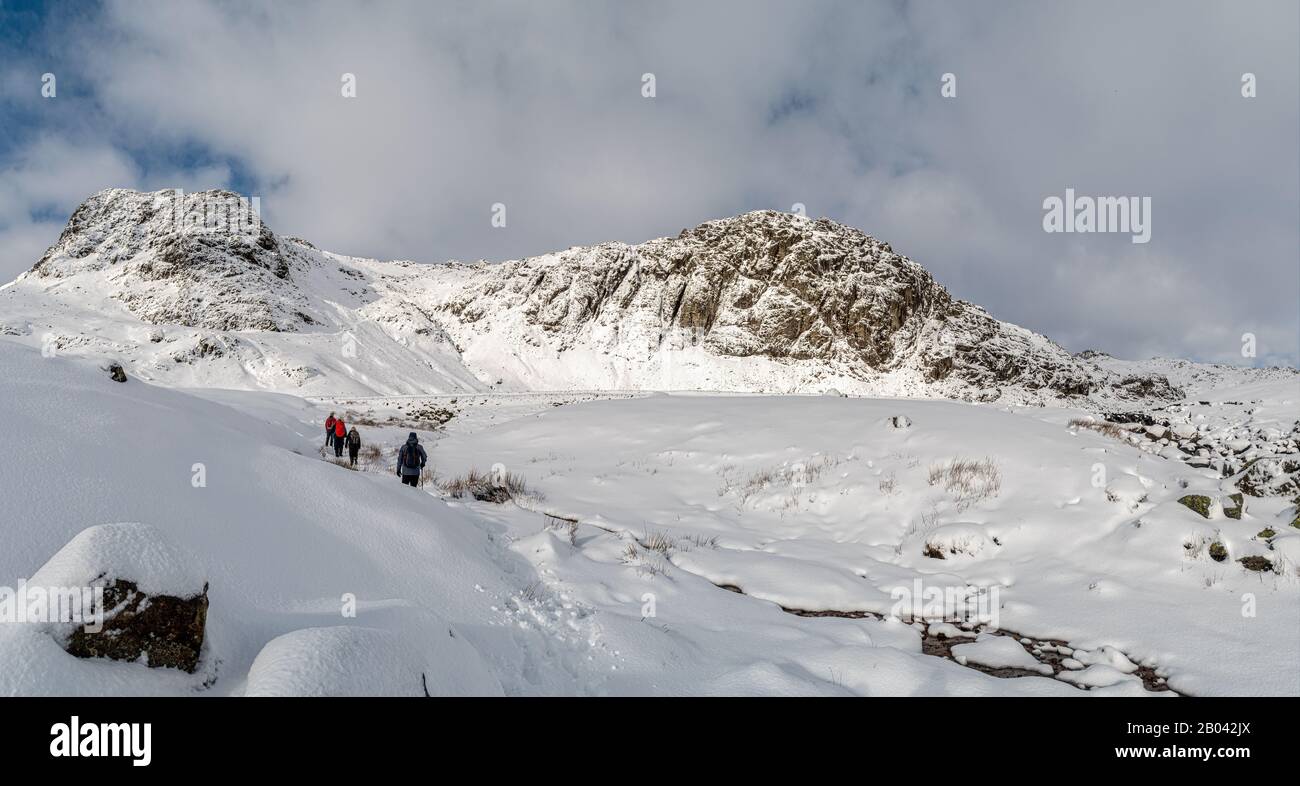 Camminatori che si avvicinano alla diga a Stickle Tarn dalla cima di Stickle Ghyll in neve fresca Foto Stock