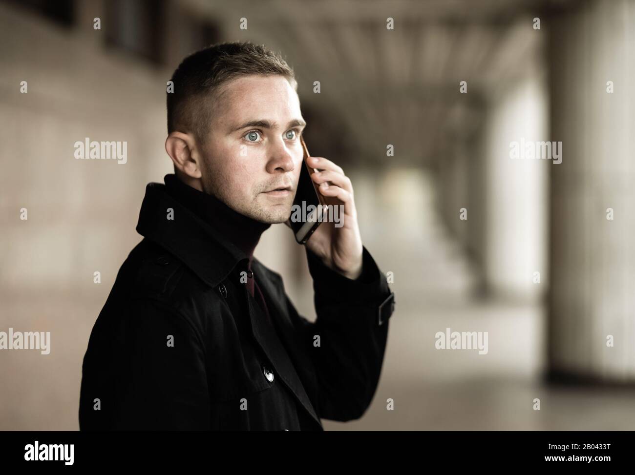 Uomo elegante con trench e polo neri che parla su un telefono cellulare Foto Stock