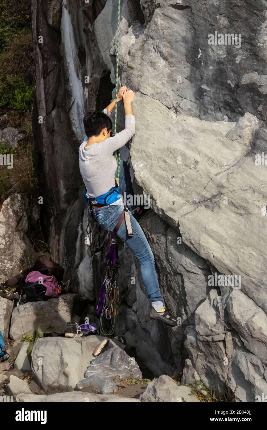 Ragazza inidentificabile con capelli molto corti che arrampicano una scogliera di roccia e scarpe e abbigliamento sparsi sulle rocce Foto Stock